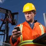 Oil miner holding a laptop looks at his mobile phone.