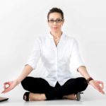A business woman sits in the lotus yoga position near her laptop, indicating a patient investment style