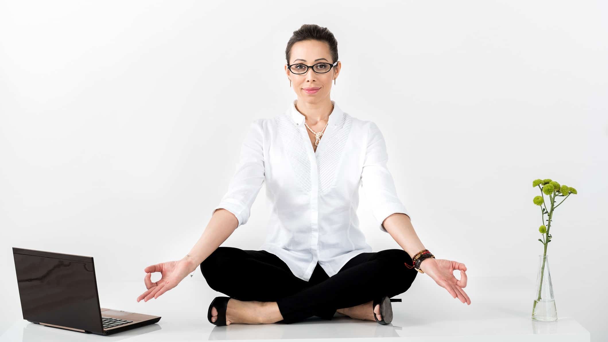 A business woman sits in the lotus yoga position near her laptop, indicating a patient investment style