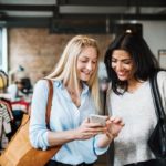 2 smiling women looking at a phone.