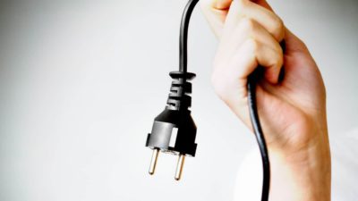 A hand holds onto the end of a power cord with a dangling plug