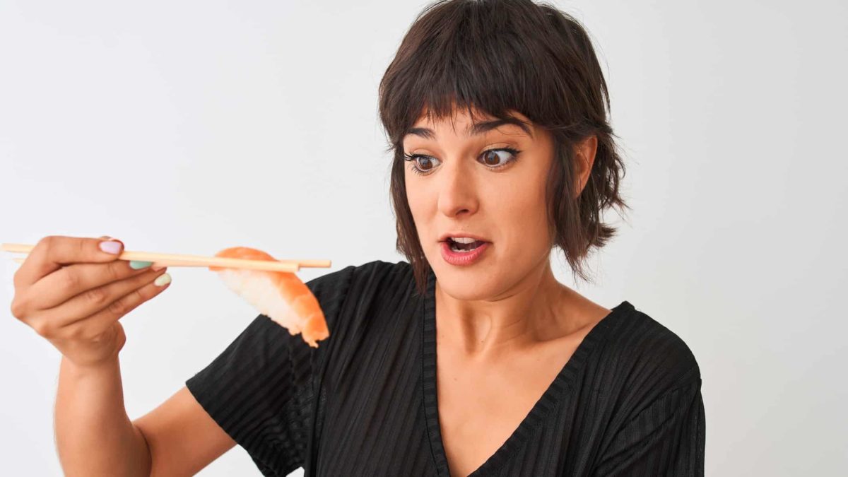 A surprised woman holds a piece of salmon with chopsticks