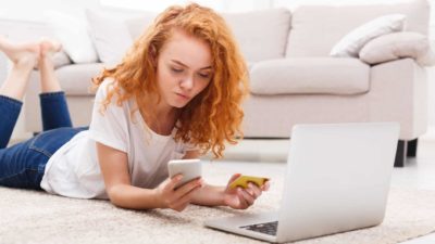 woman lays on floor with laptop and looks anxious while using credit card