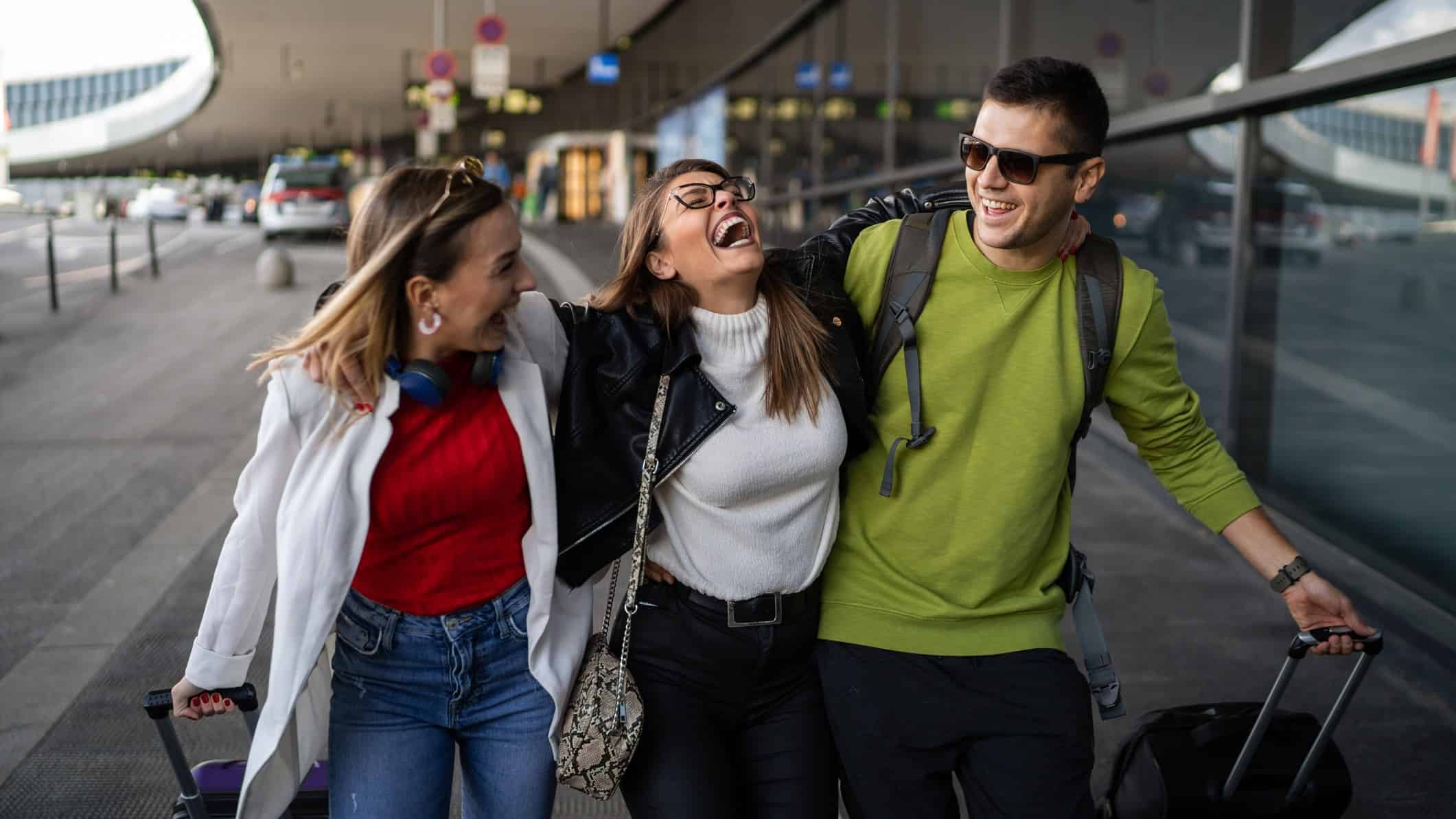 Three travellers laughing and smiling outside an airport