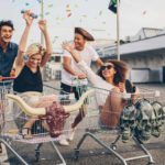 Two couples race each other in supermarket trollies, having a great time, smiling and laughing.