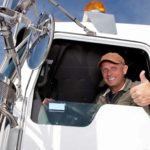 A truck driver leans out the window of his truck giving the thumbs up.