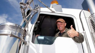 A truck driver leans out the window of his truck giving the thumbs up.