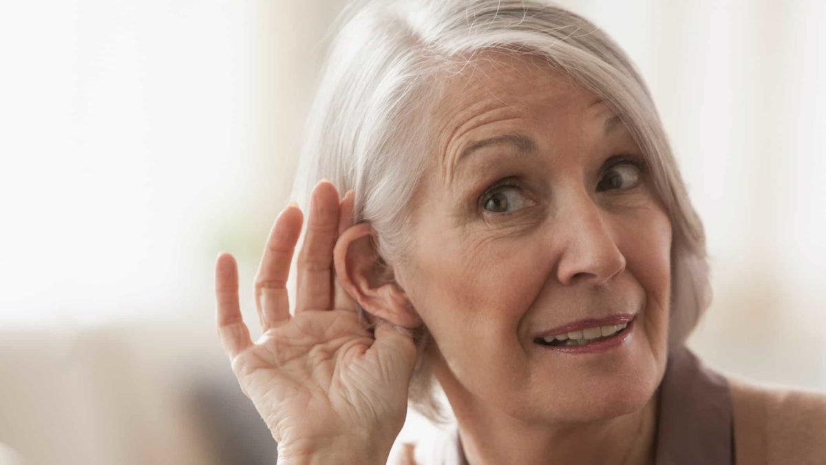 An older woman tries to listen by cupping her ear.