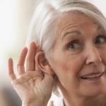 An older woman tries to listen by cupping her ear.