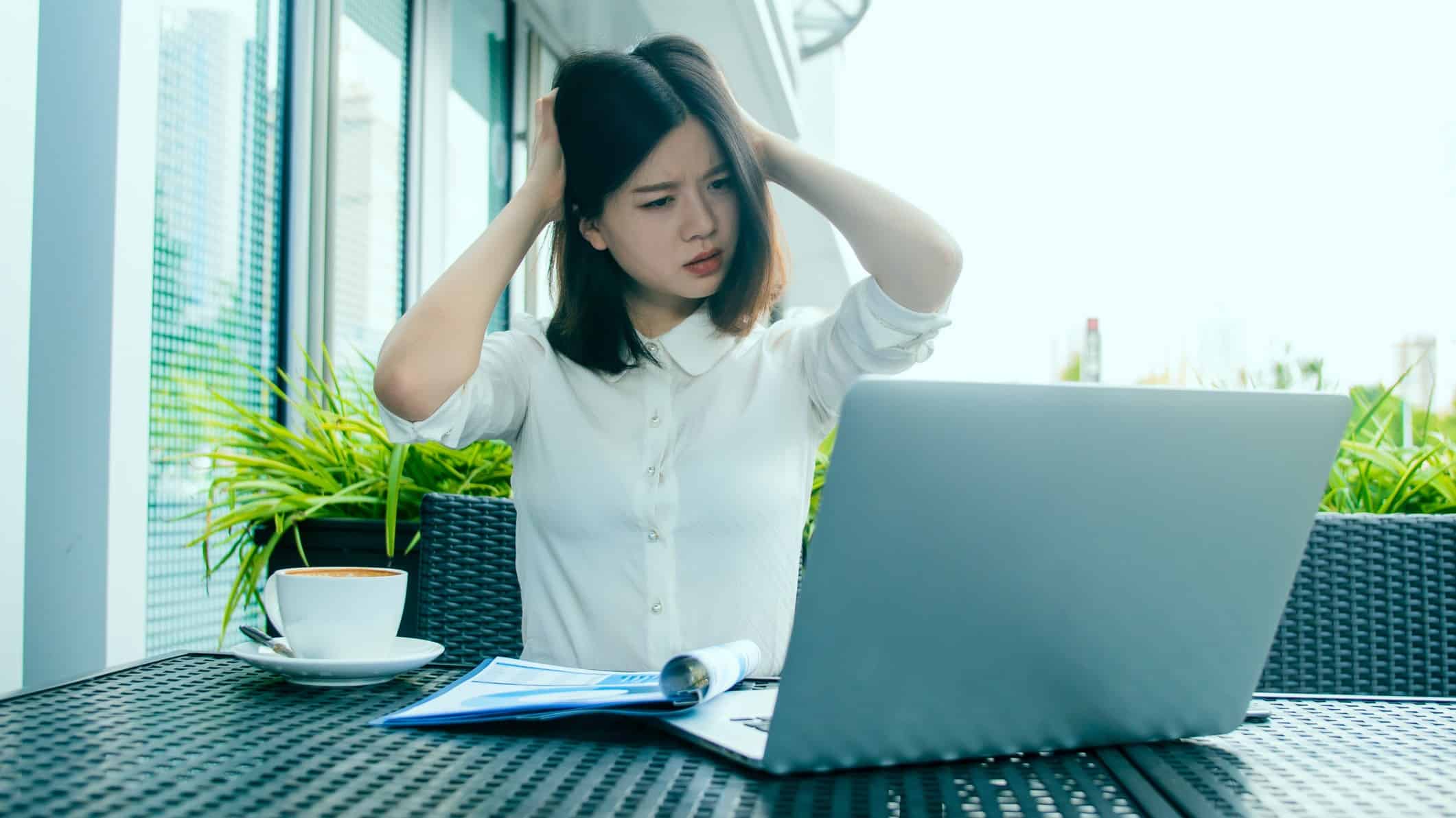 Woman sits at laptop looking confused and stressed