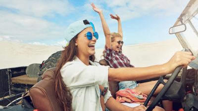 Two women in a 4WD vehicle with Carbon Revolution wheels drive along laughing with one throwing her arms in the air