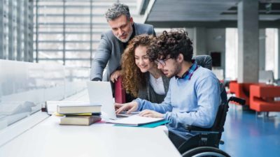 Two university students in the library, one in a wheelchair, log in for the first time with the help of a lecturer.