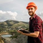 A miner in a hardhat makes a sale on his tablet in the field.