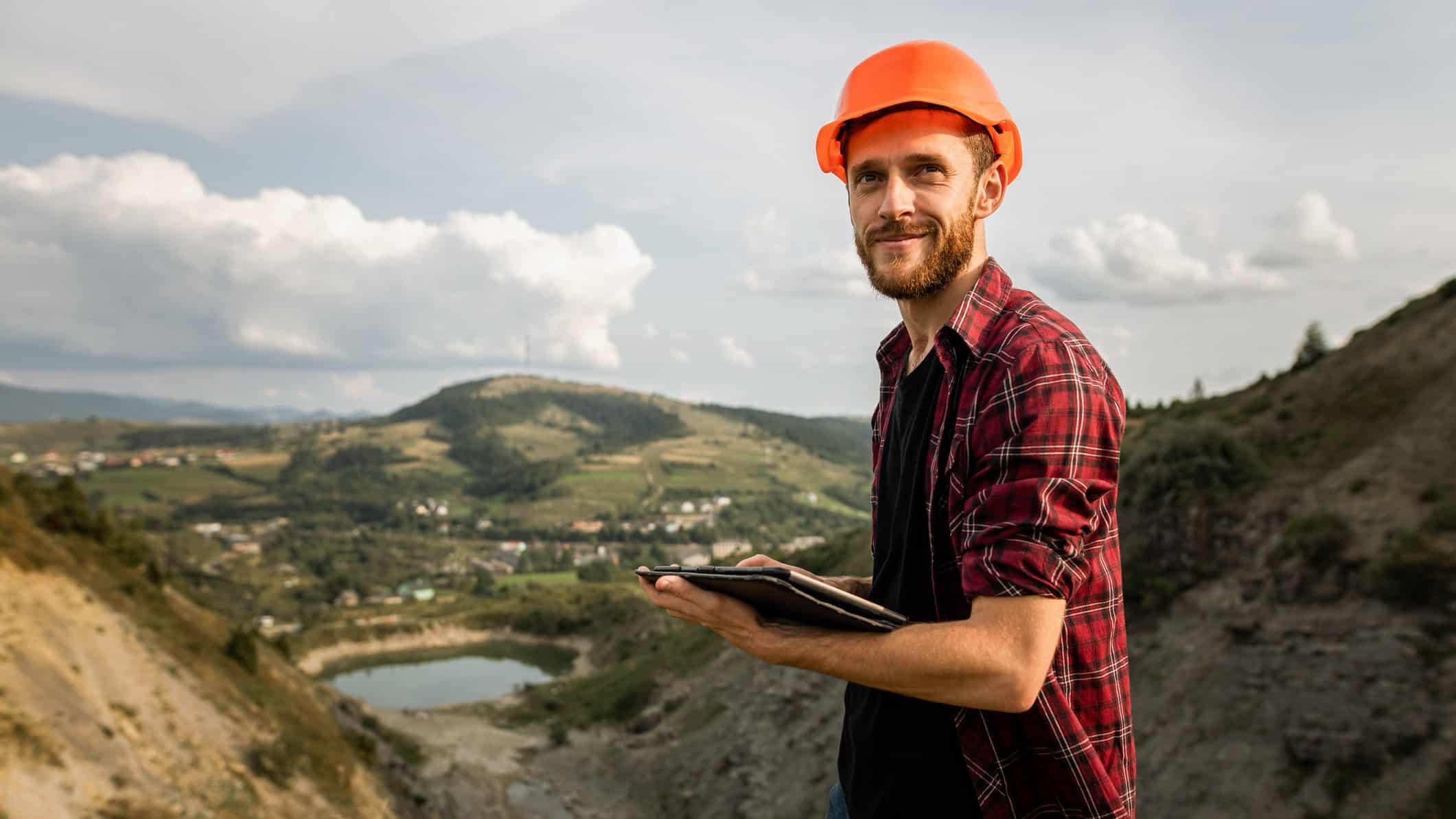 A miner in a hardhat makes a sale on his tablet in the field.