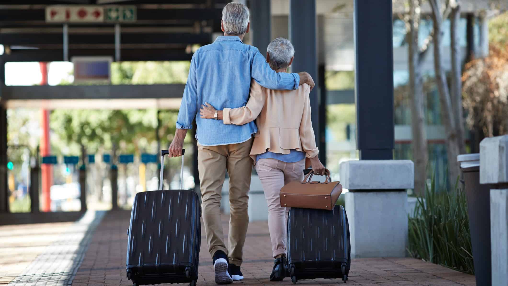 A couple merge carrying suitcases arm in arm at the airport.
