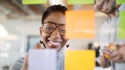 A woman is happy about the ideas she and her colleague are coming up with, and writing on post-it notes.
