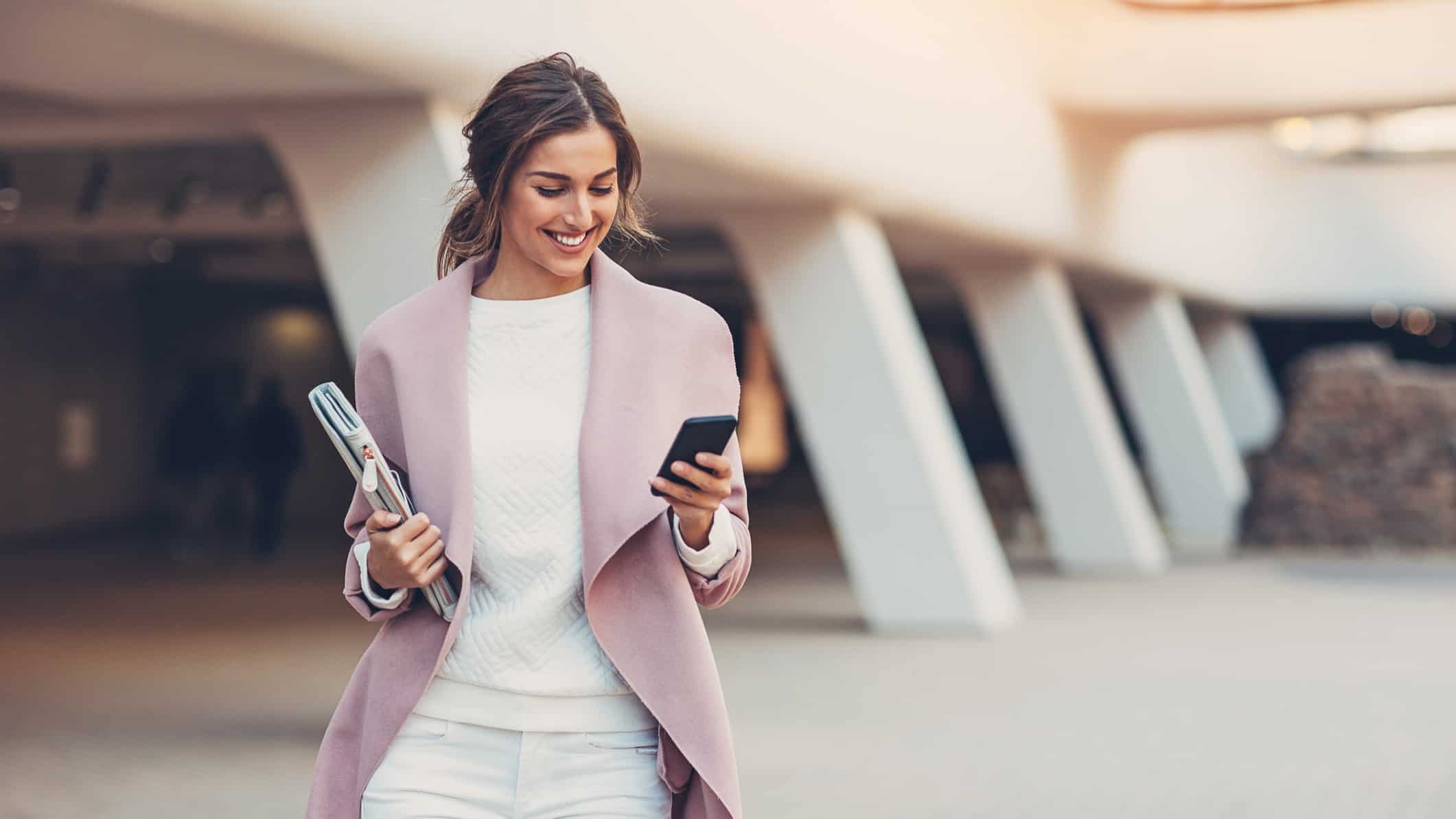 A smartly-dressed businesswoman walks outside while making a trade on her mobile phone.