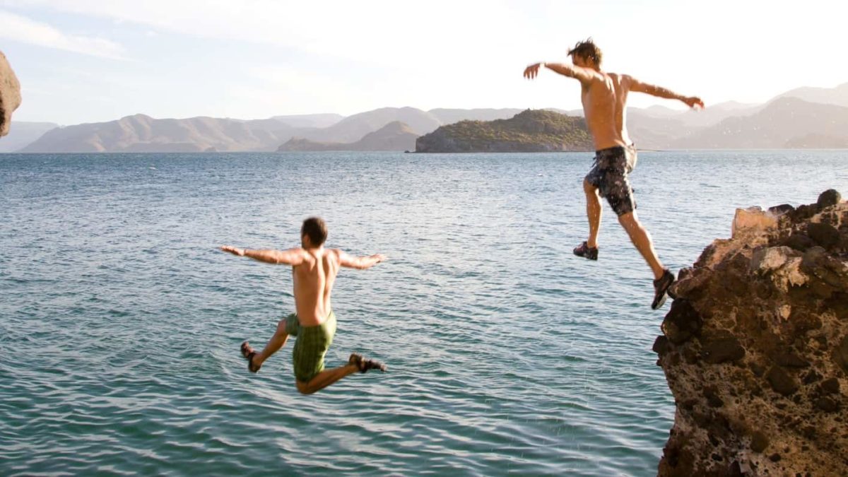 Two young men jump off a cliff into the water.