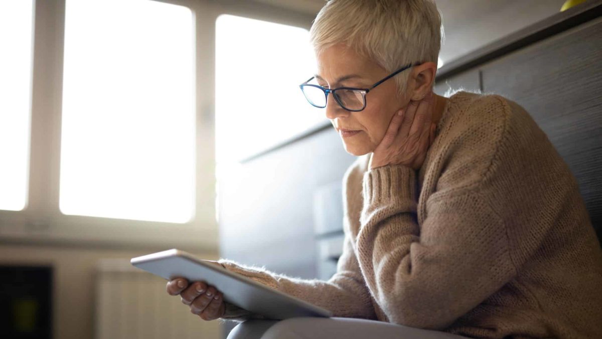 A middle-aged woman sits in contemplation over a tablet device considering information about ASX shares and deep in thought.