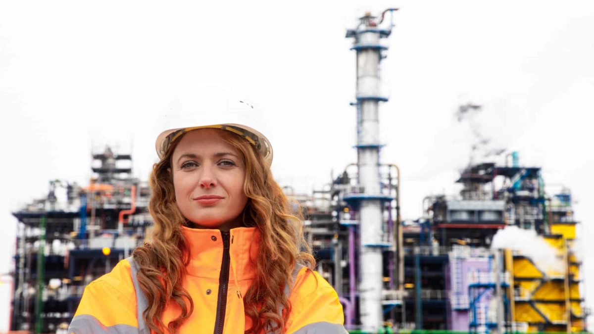 a woman in high visibility clothing and a hard hat stands in front of an aluminium smelter.