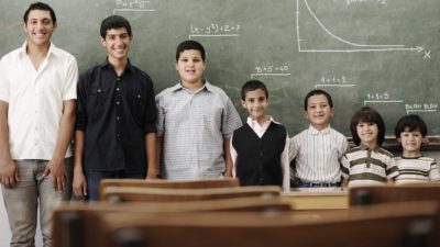a line up of young boys from tallest to shortest against a blackboard where a mathematical equation appears written above each of their heads.