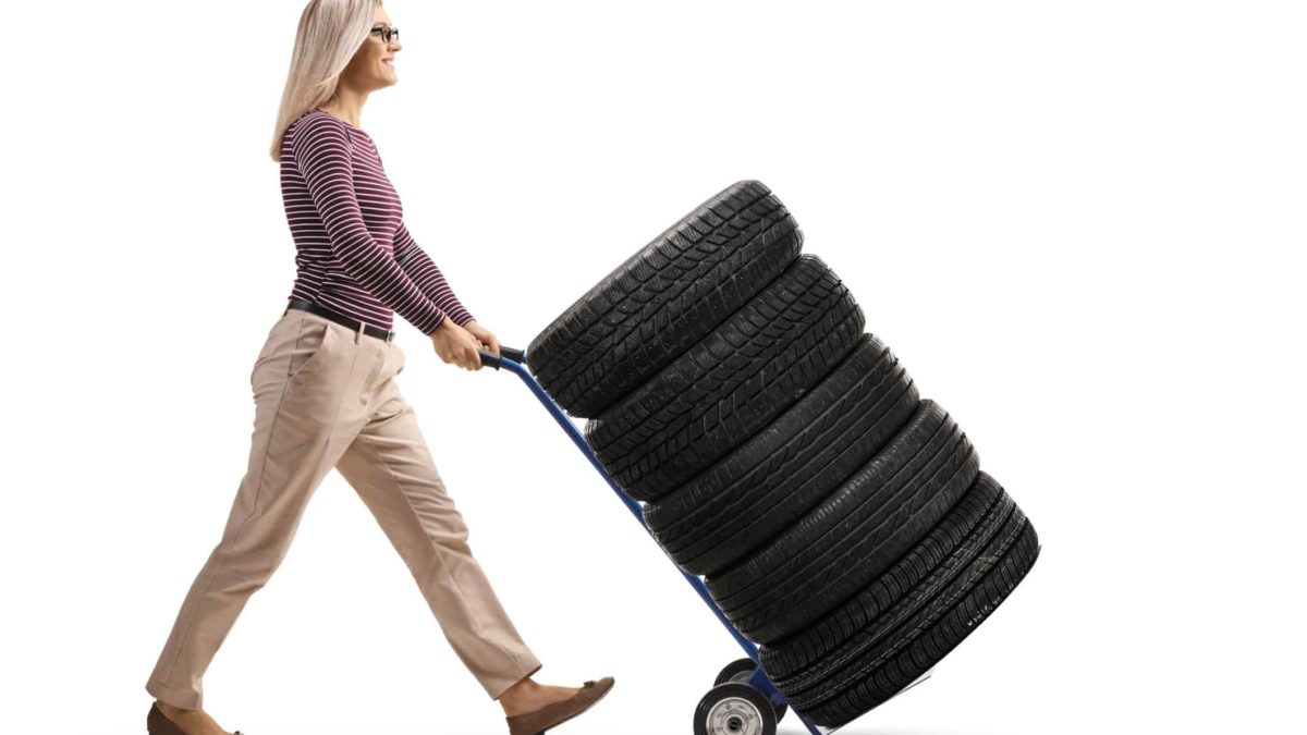 a woman wheels five rubber car tyres piled onto a trolley.