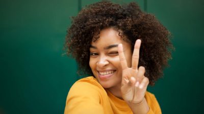 a smiling woman holds up two fingers and winks.