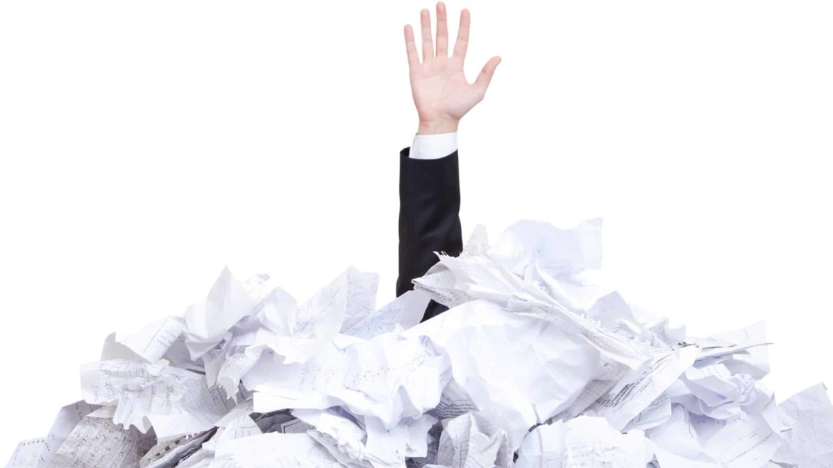 a hand reaches up from a large pile of papers.