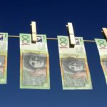 four one hundred dollar bills hang on a washing line with old-fashioned wooden pegs, denoting money laundering.