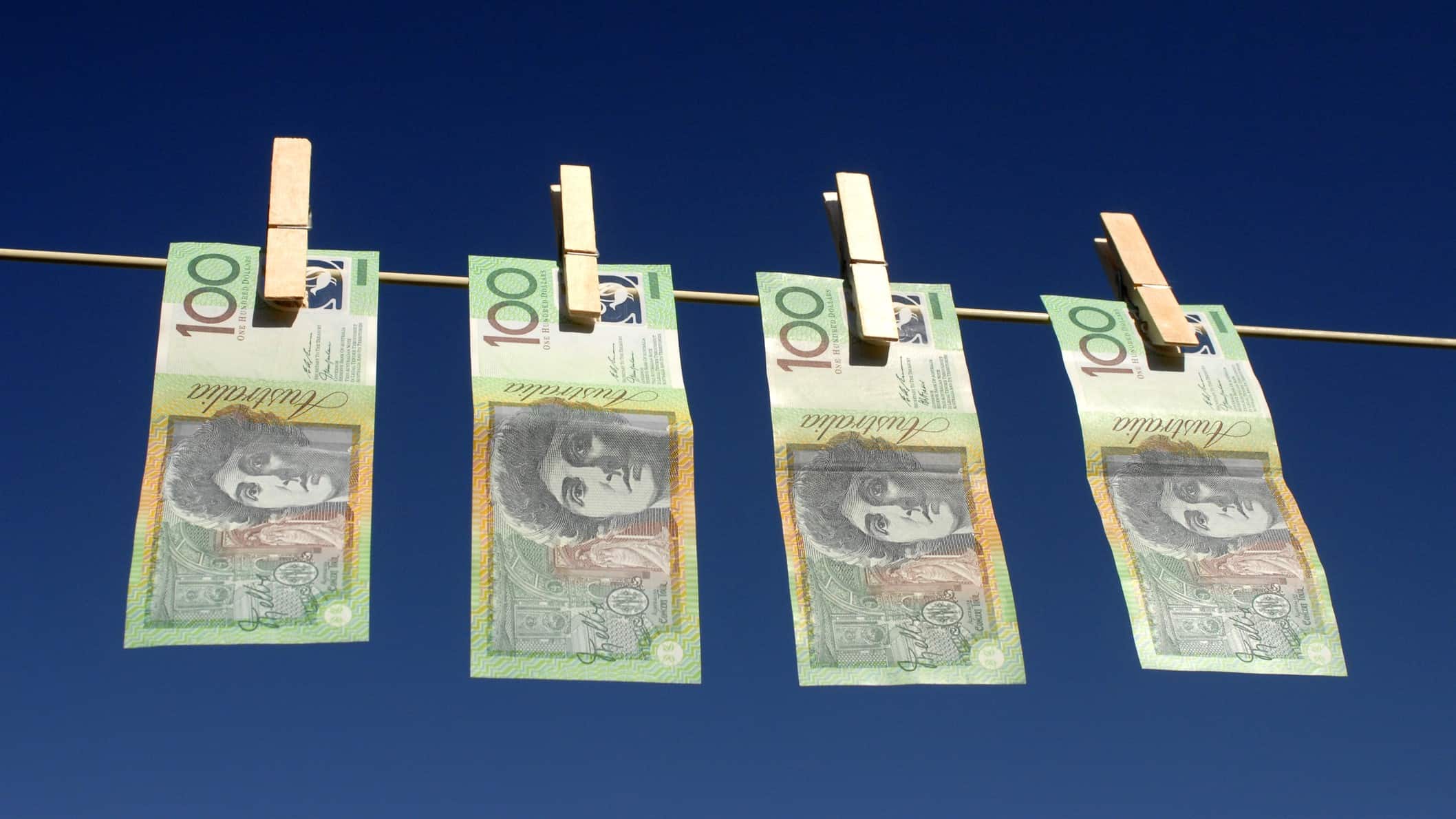 four one hundred dollar bills hang on a washing line with old-fashioned wooden pegs, denoting money laundering.