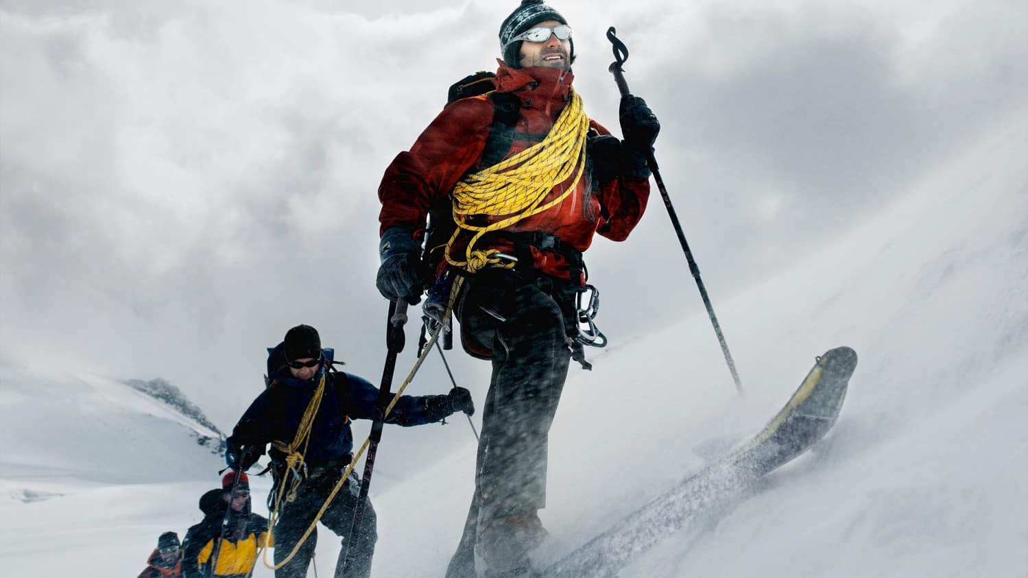 a cross country skier leads three others up an incline amid cold and snowy conditions in a snowy mountain setting.