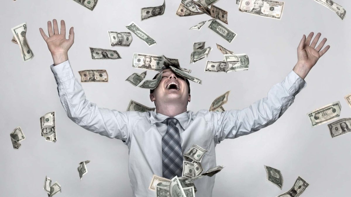 A man throws his arms up in happy celebration as a shower of money rains down on him.