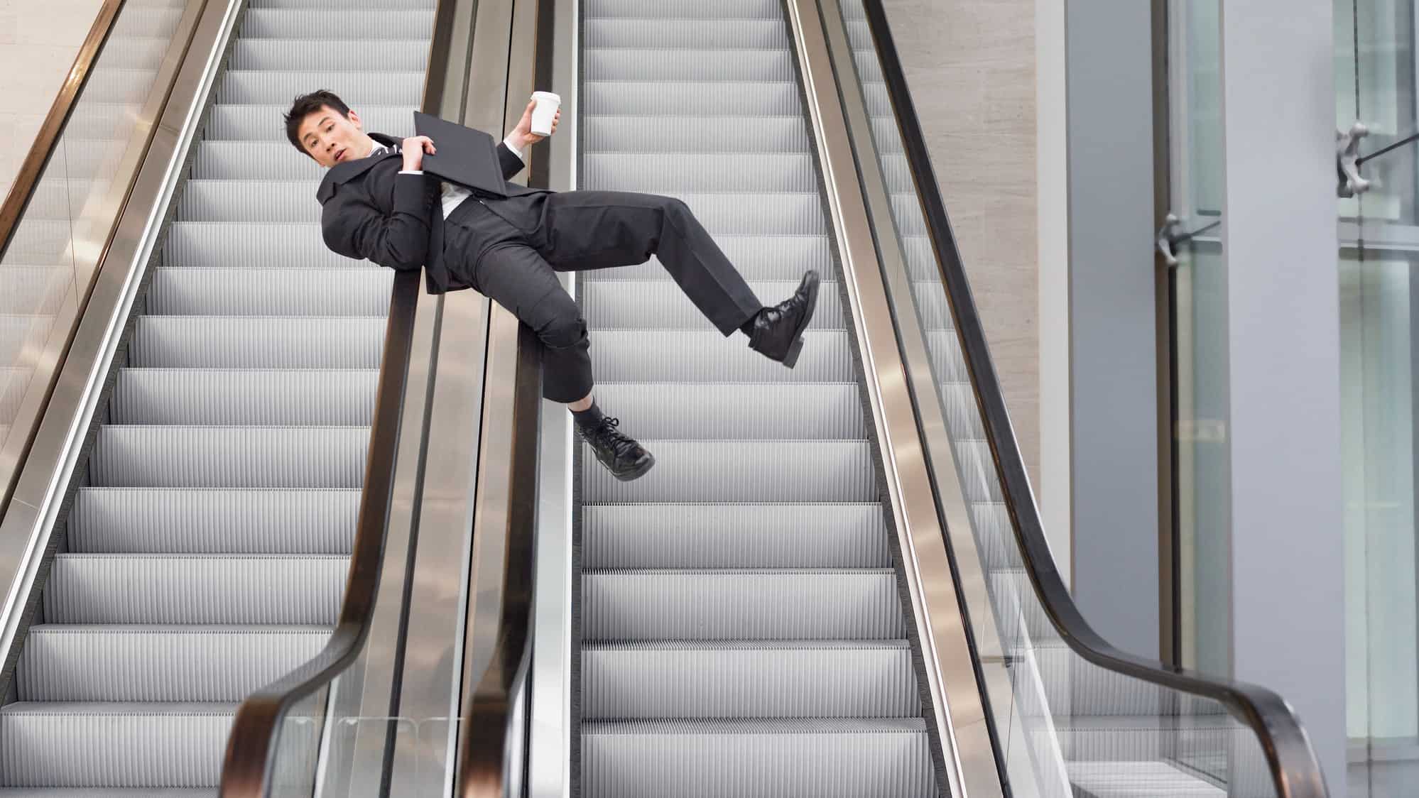 a man in a business suit slides down the handrails of a bank of steel escalators, clutching his documents and telephone.