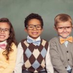 a group of smart looking kids, wearing formal clothes and all with spectacles, sit in a line and smile charmingly.