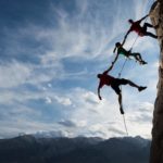 a group of rockclimbers attached to each other with a rope hang precariously from a steep cliff face with the bottom two climbers not touch the rockface but dangling in midair held only by the rope.