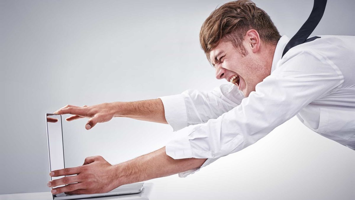 a man dressed in business clothes struggles to hold on to his computer in the face of strong headwinds.