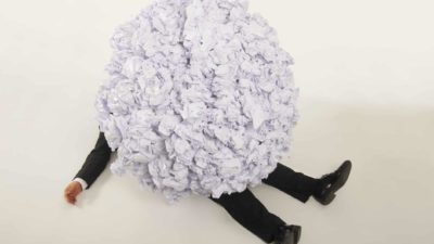 a person's legs and an arm sticks out from underneath a large ball of scrunched paper.