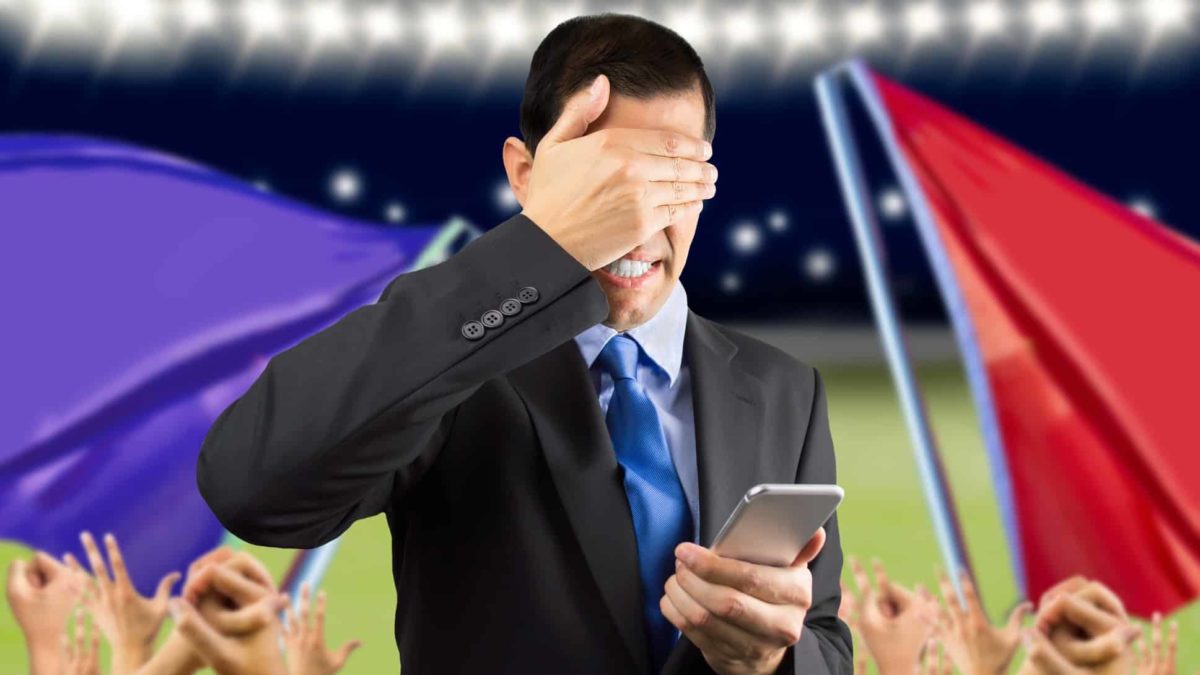 a man attending a sporting match looks down at his phone with his hand over his eyes in dismay as though his sporting bet has failed.