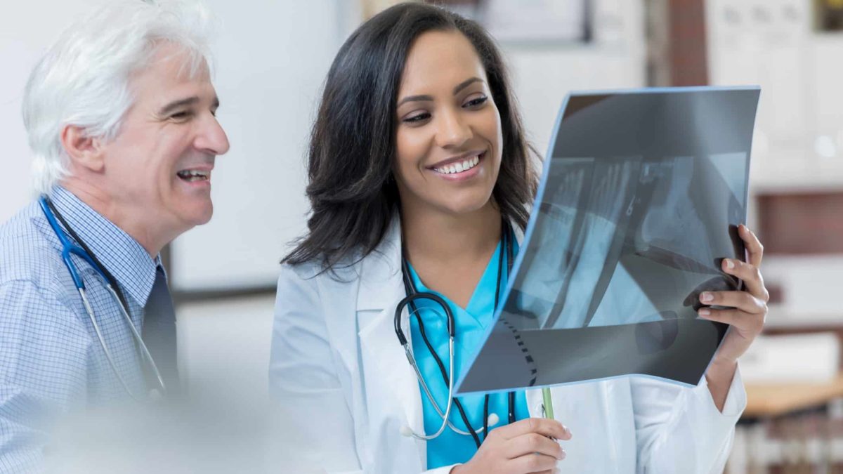 two doctors smile as they sit together at a desk looking at a patient's Xray.