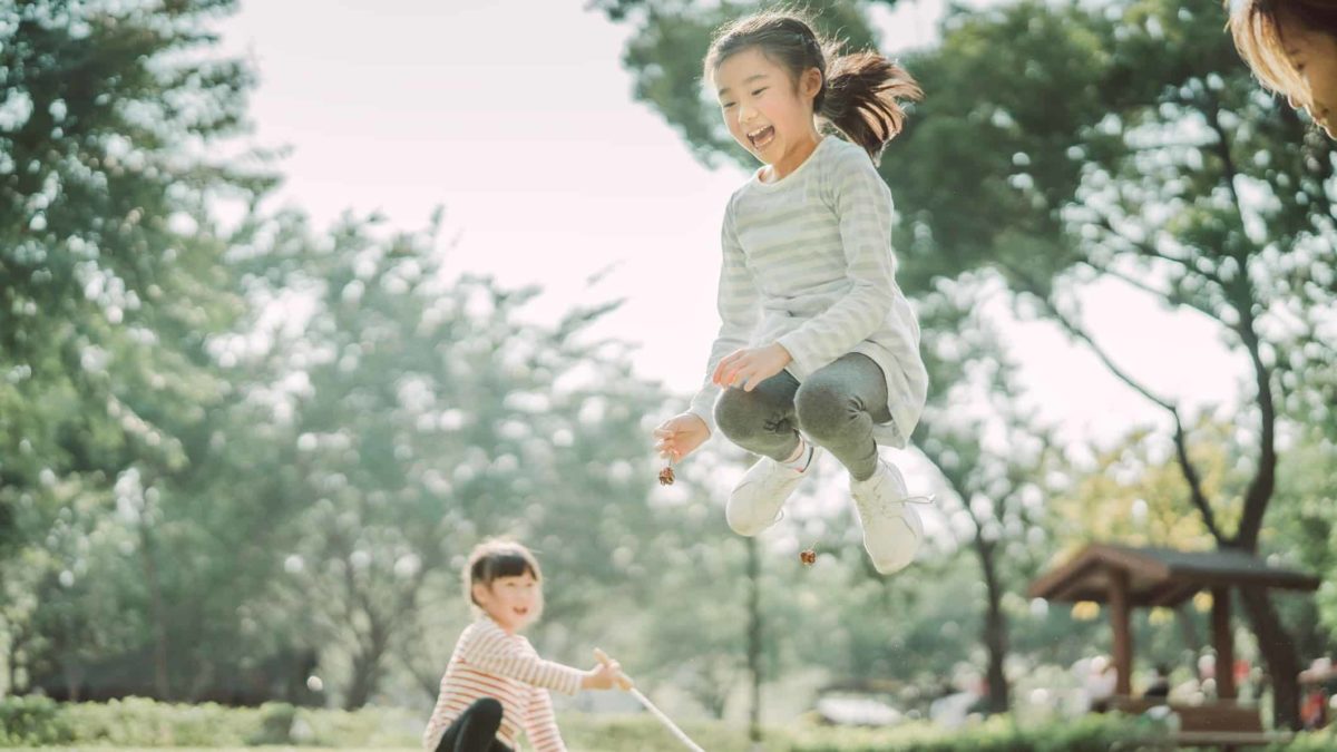 A girl jumps high over a skipping rope in a garden.