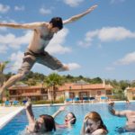 A man leaps as high as he can over his friends into a pool.