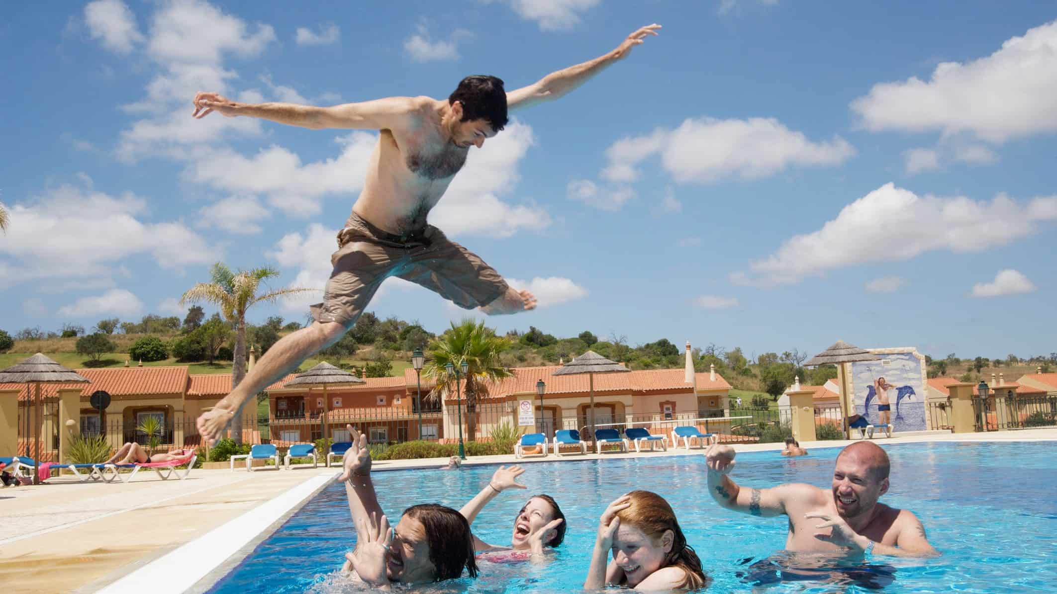 A man leaps as high as he can over his friends into a pool.
