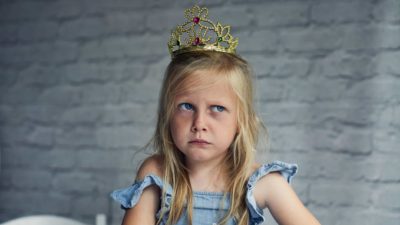 A little girl looks grumpy about the crown upon her head.