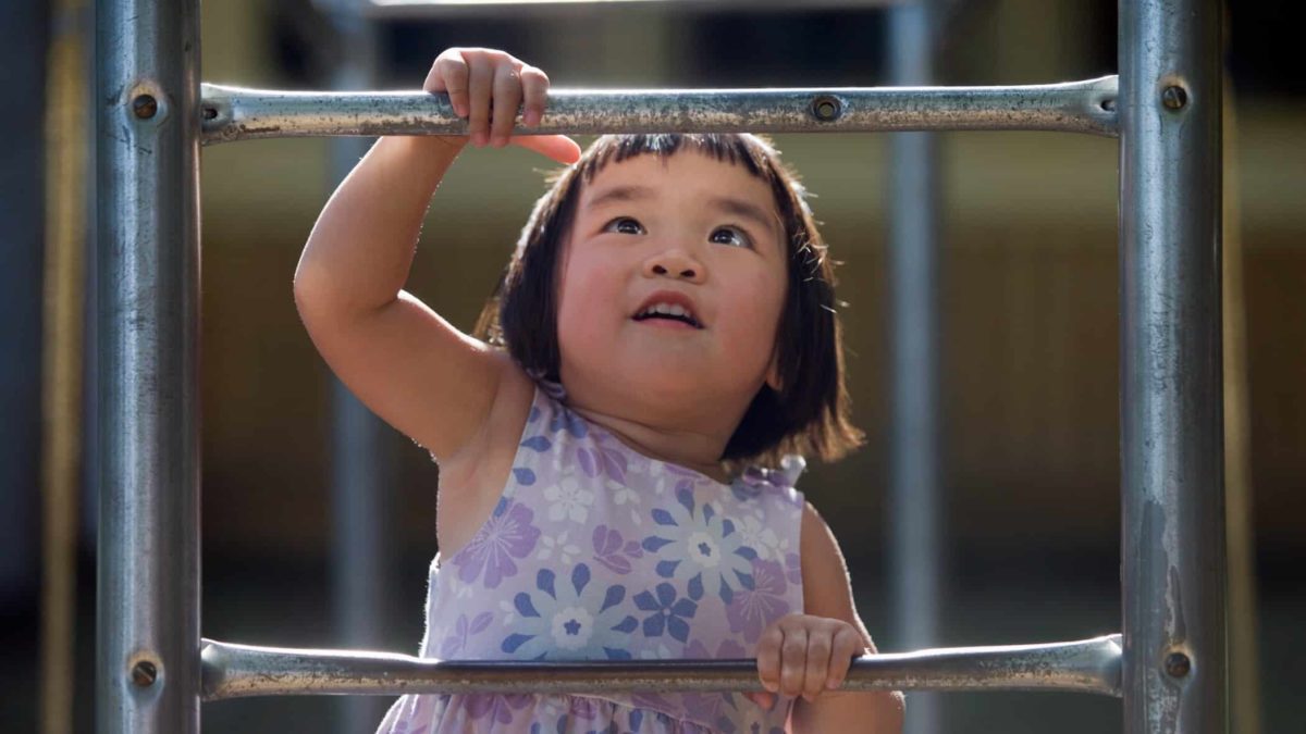 A little Asian girl climbs a metal ladder in the playground.