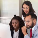 Three colleagues stare at a computer screen with serious looks on their faces.