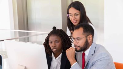 Three colleagues stare at a computer screen with serious looks on their faces.