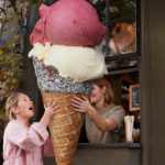 A girl is handed an oversized ice cream cone with lots of different flavours.