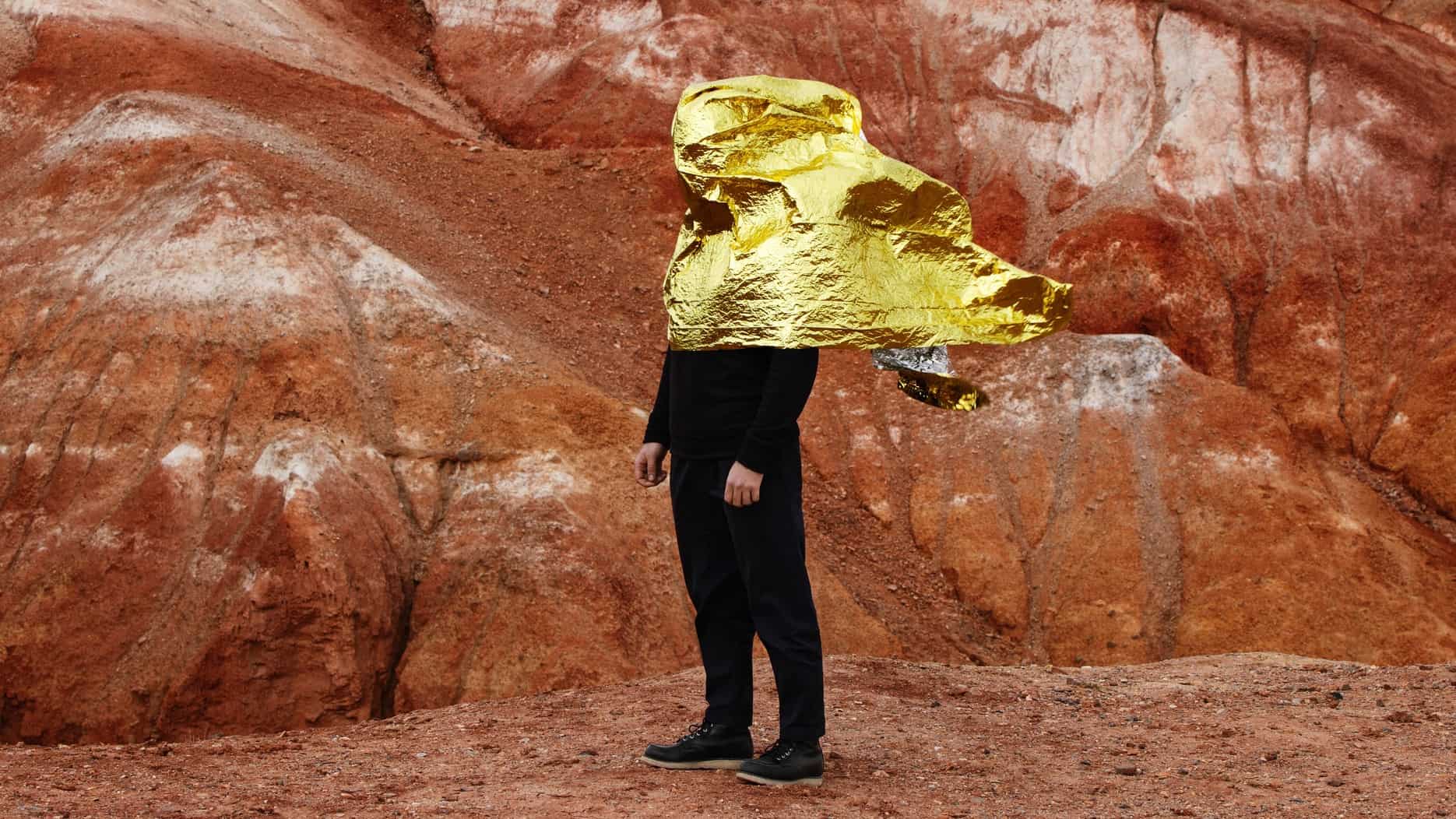 A man standing in a red rock mine is covered by a sheet of gold blowing in the wind.