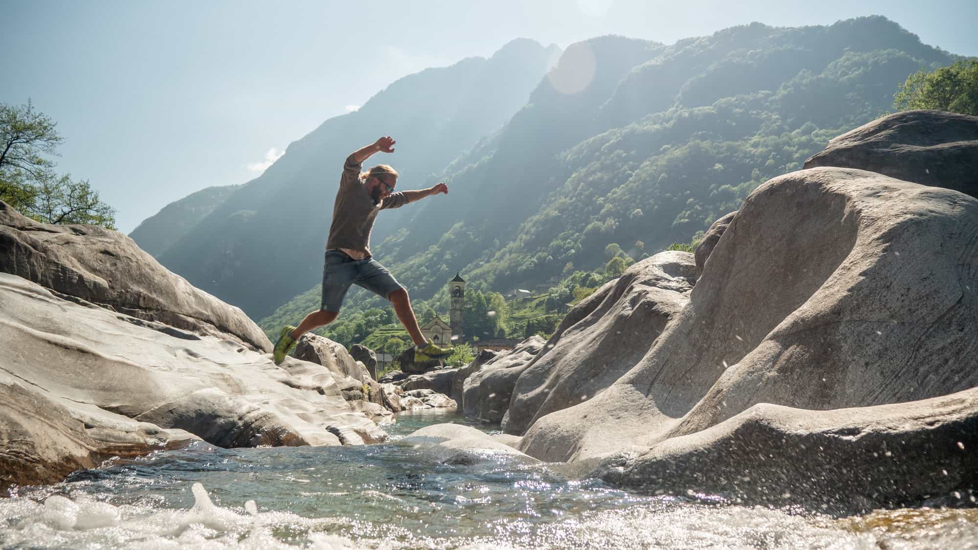 A man jumps over a river, bouncing from one rock to another.
