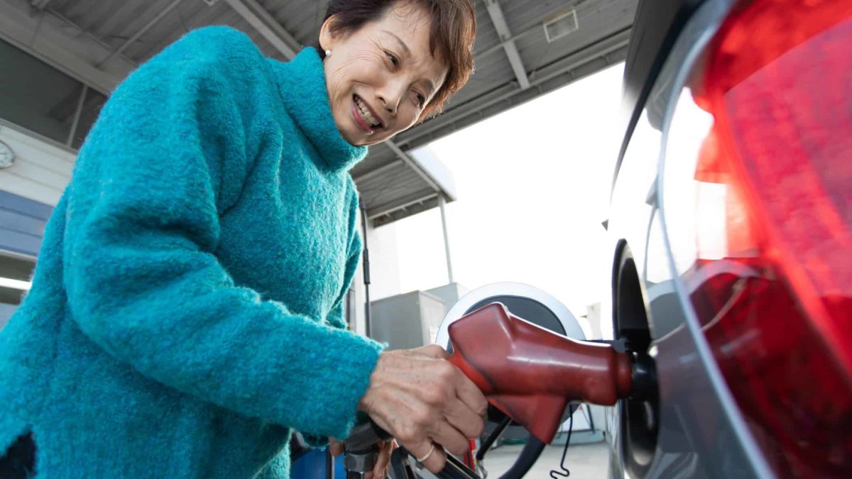 An older Asian woman fills up her car with petrol at the service station.